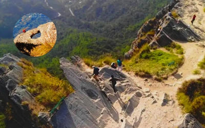 Rocky cliff face with a natural circular hole ('Jali') where people are climbing and enjoying the view